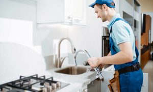 plumber in uniform changes faucet in the kitchen